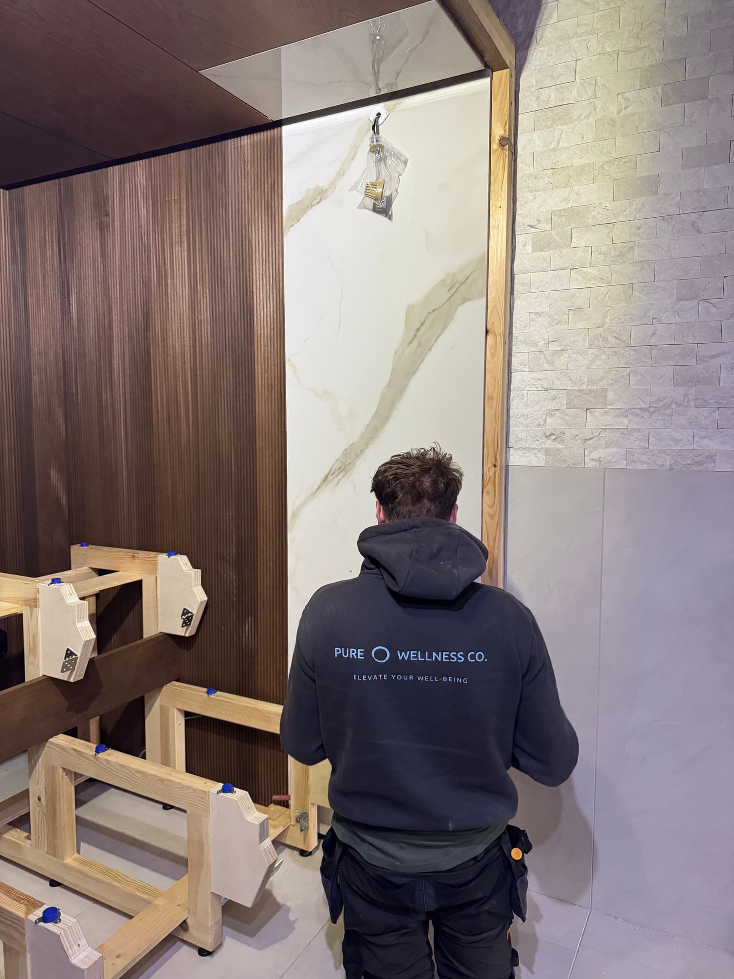 Pure Wellness installer fitting the sauna interior beside exposed bench supports