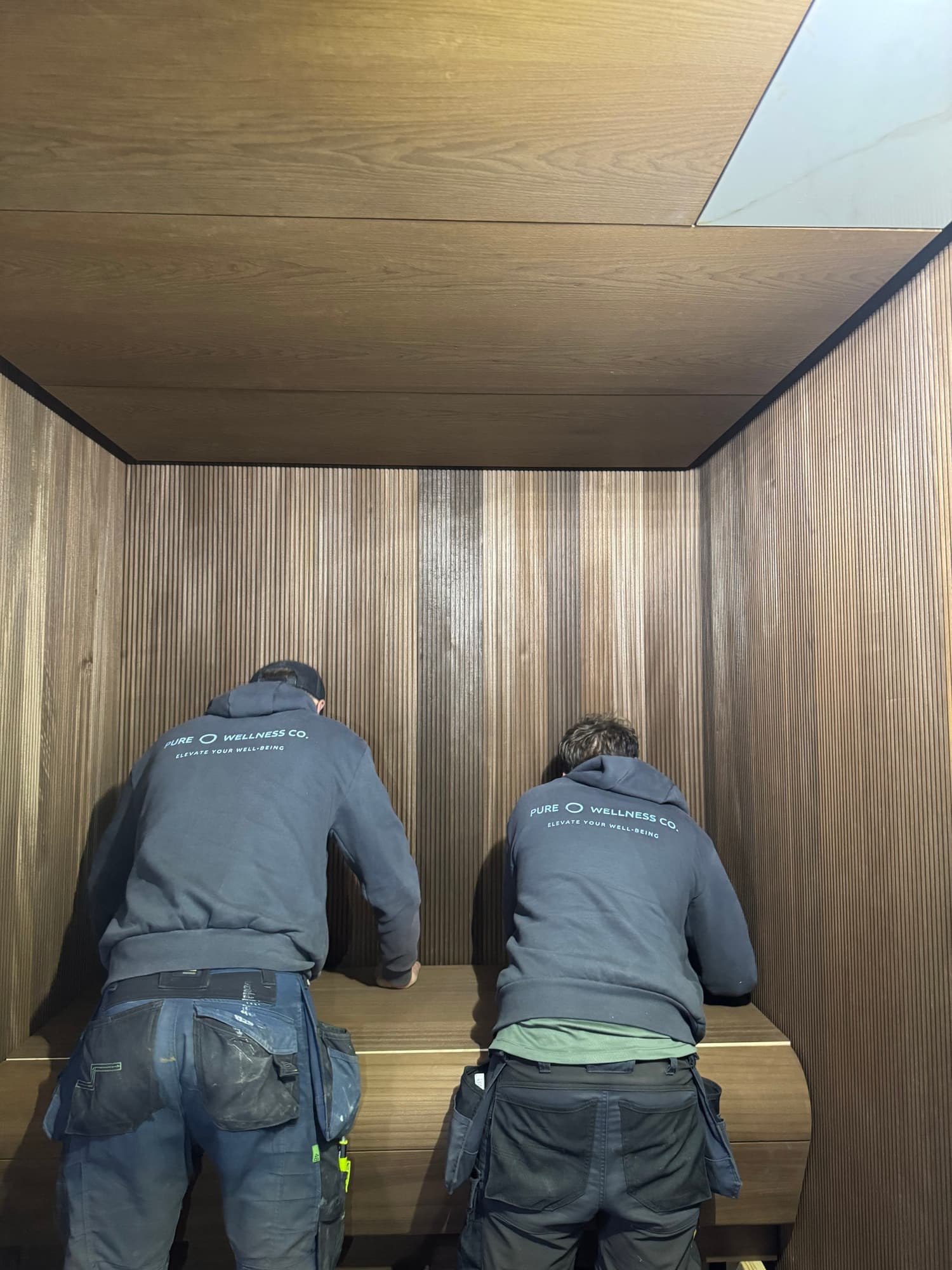 Two Pure Wellness installers positioning a curved sauna bench