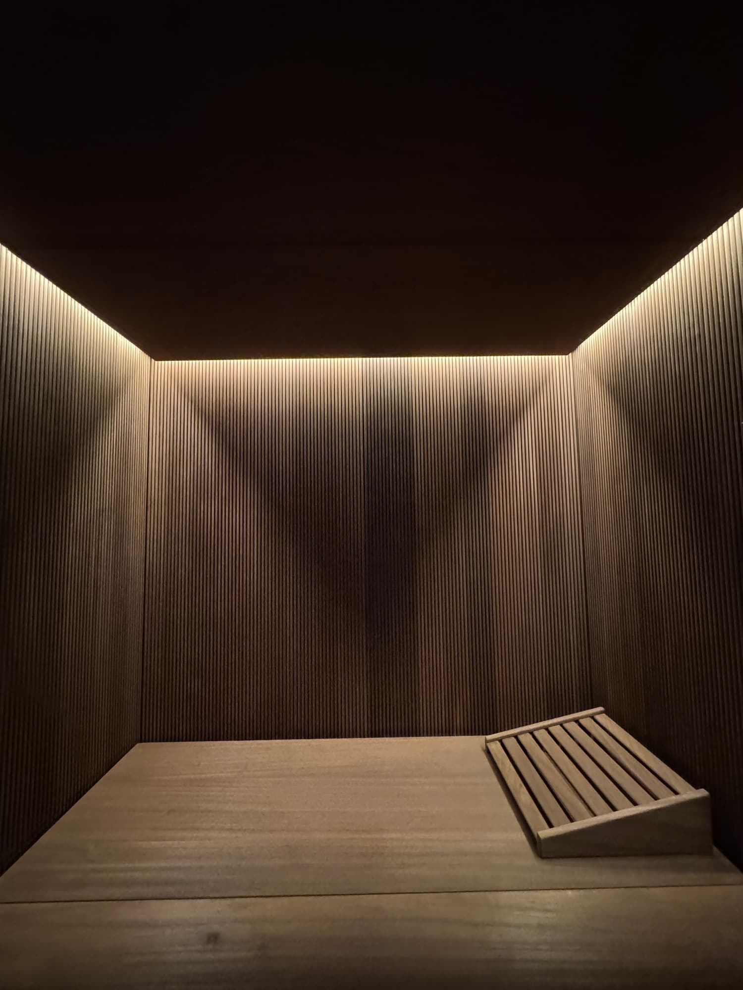 Finished curved sauna bench beneath warm concealed ceiling lighting