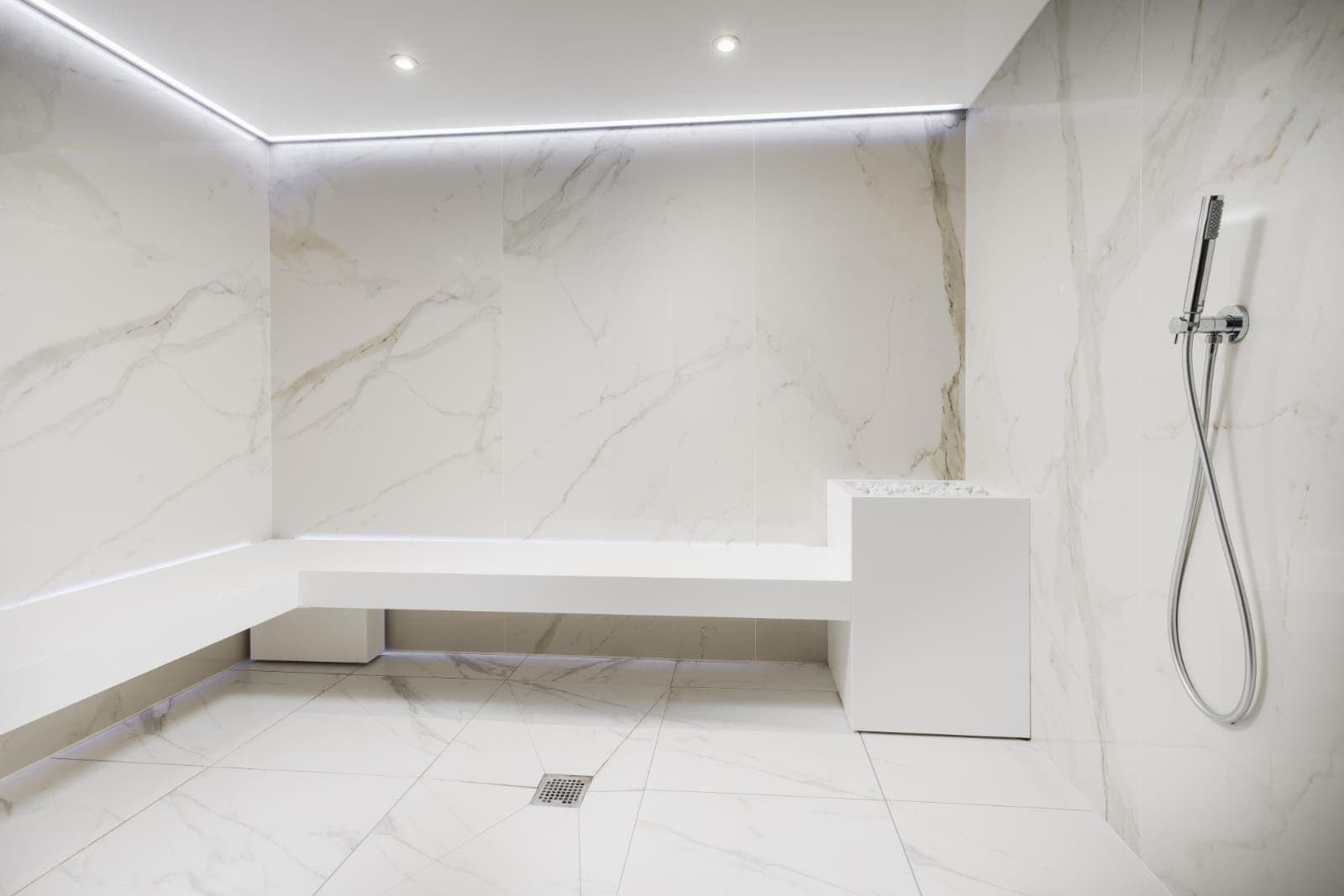 Shower area with dark tiling, brushed metal fittings and recessed lighting