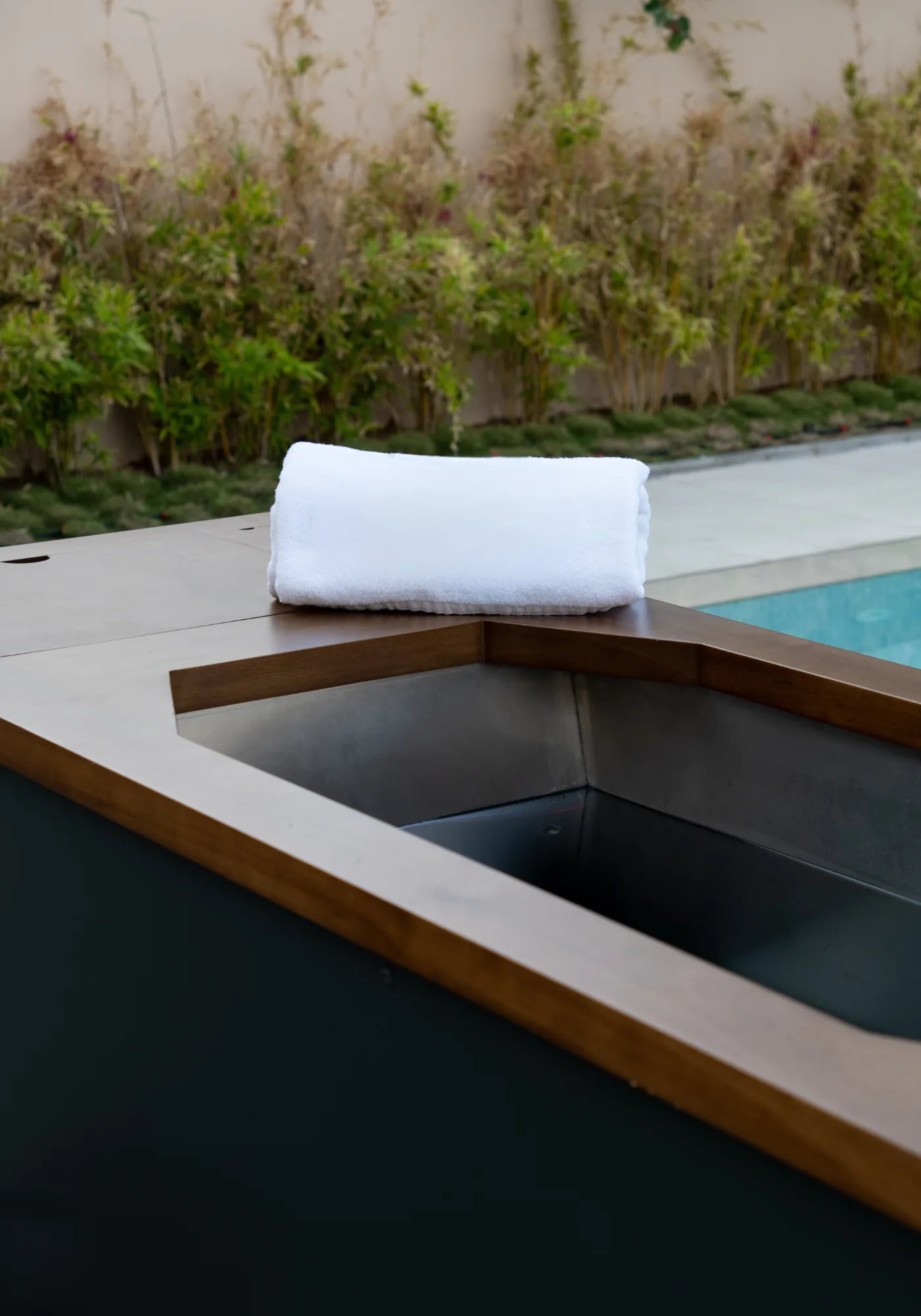 Nebula ice bath installed beside a pool, towel folded on the teak rim