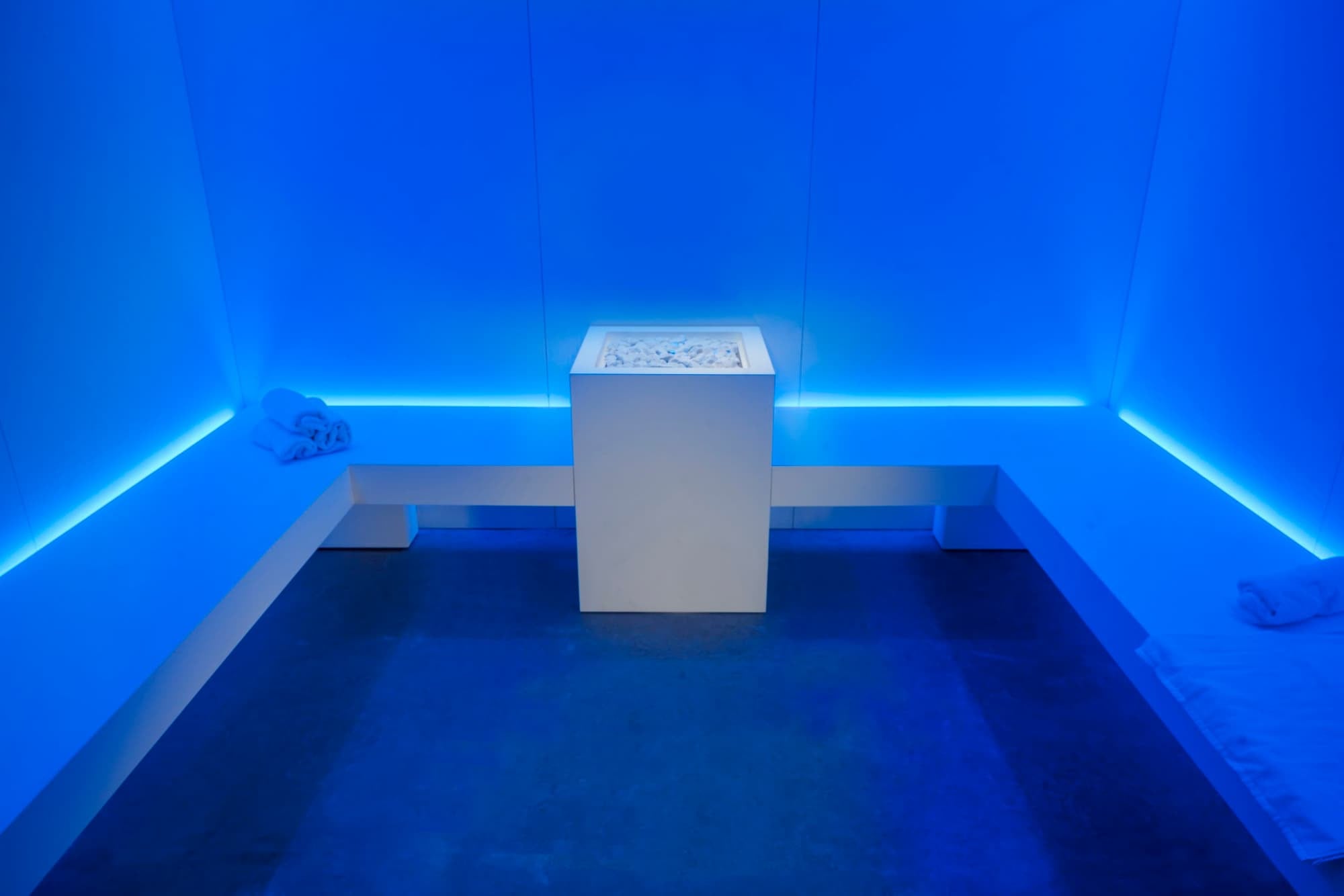 Minimalist spa room with blue LED lighting, a central pedestal and folded towels on corner benches