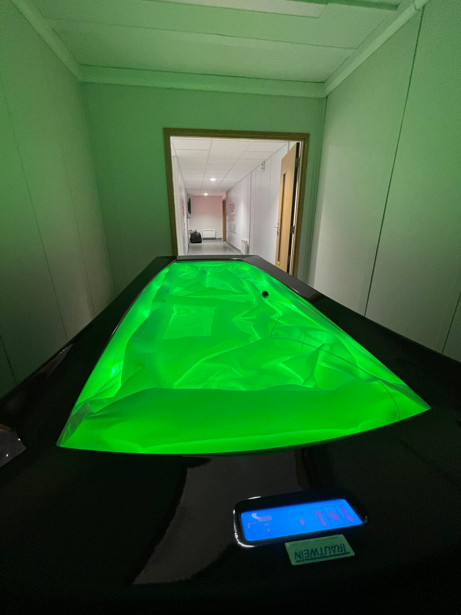 An indoor room with a ping pong table illuminated with green light, a phone with a blue screen on the table, and a door leading to a hallway.