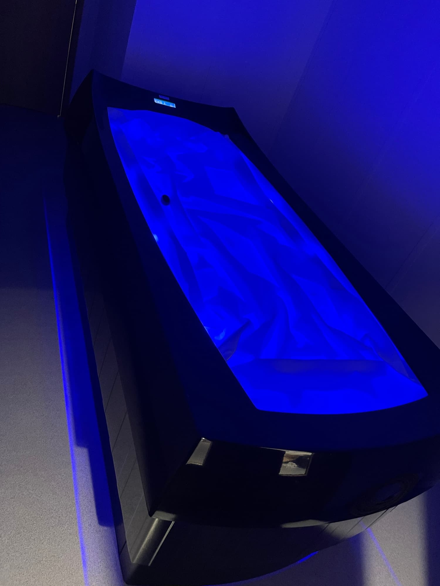 A modern curved hot tub with blue lighting, situated indoors on a tiled floor.