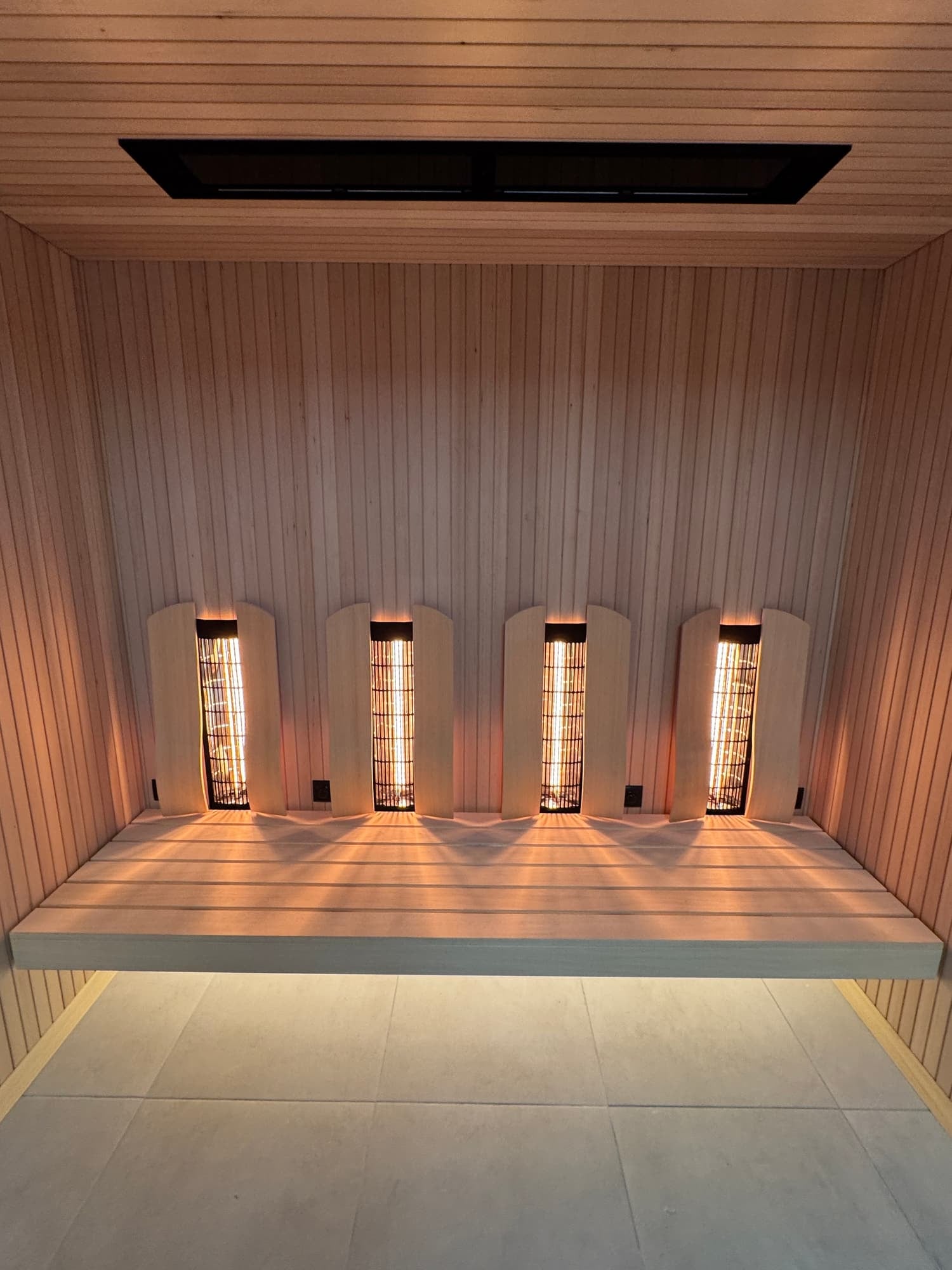 Interior of a room with wooden walls and ceiling, featuring five infrared lamps and a wooden bench.