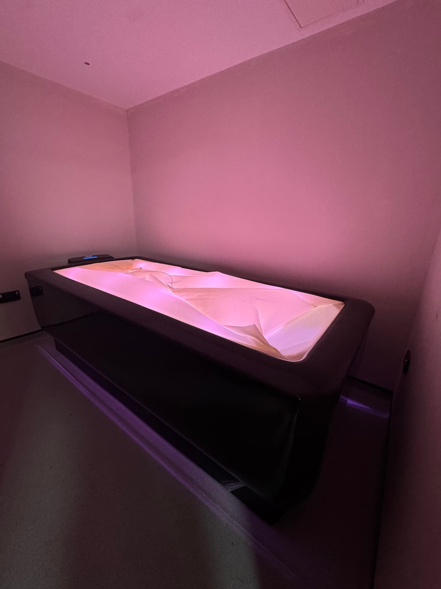 A modern tanning bed with pink illumination in a minimalistic room.