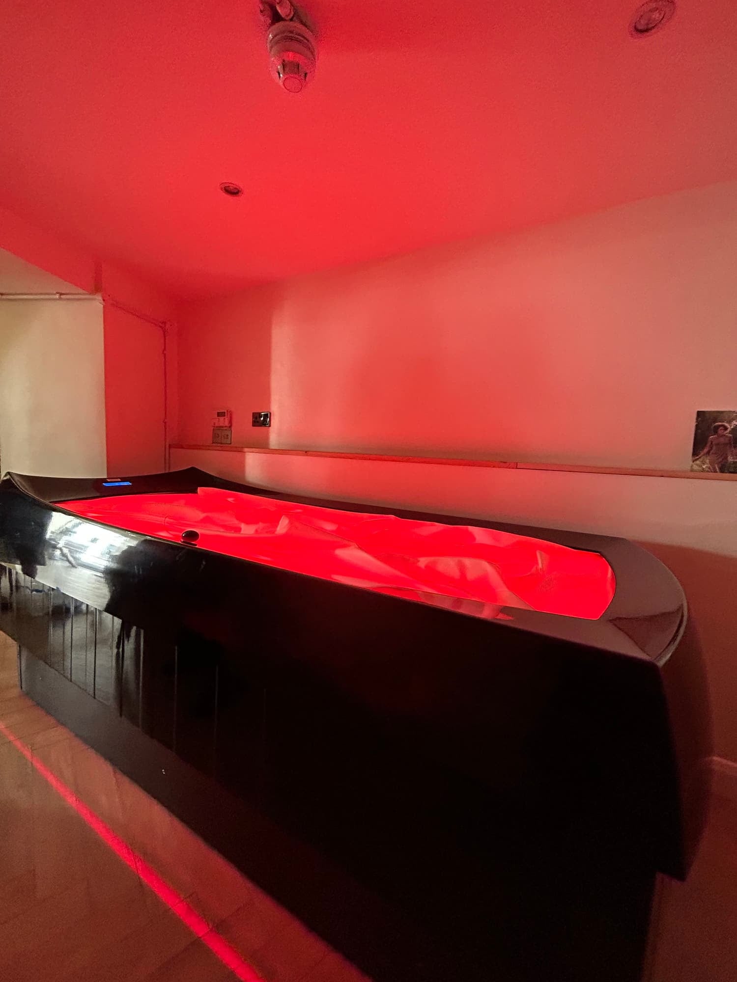 An indoor spa with a large, black jacuzzi tub filled with red-colored water, illuminated by red lighting.