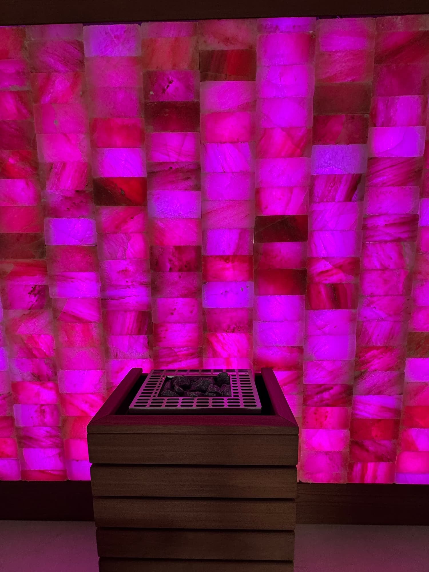 Illuminated Himalayan salt wall behind a guarded sauna heater